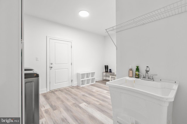 washroom with a sink, light wood finished floors, laundry area, and baseboards