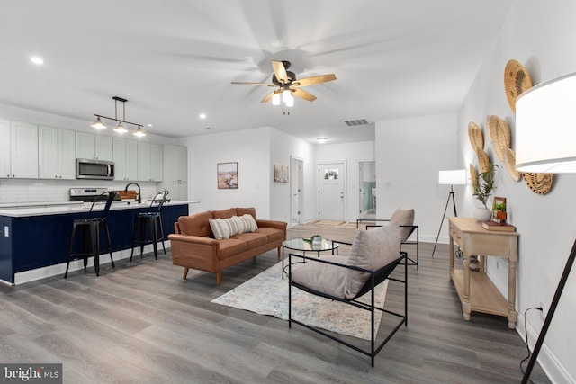 living room with ceiling fan, visible vents, baseboards, light wood-type flooring, and recessed lighting