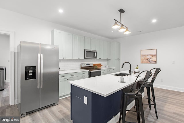 kitchen featuring hanging light fixtures, an island with sink, a sink, light countertops, and appliances with stainless steel finishes