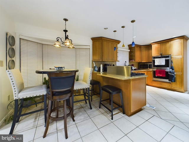 kitchen featuring pendant lighting, a breakfast bar area, brown cabinetry, appliances with stainless steel finishes, and a peninsula