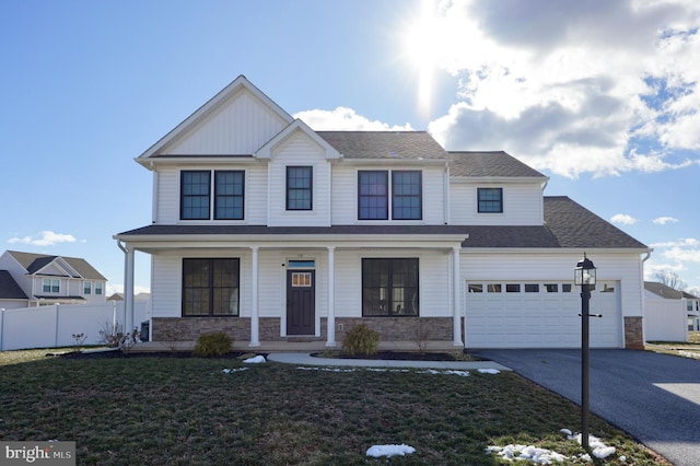 view of front of house featuring covered porch, fence, a front lawn, stone siding, and aphalt driveway