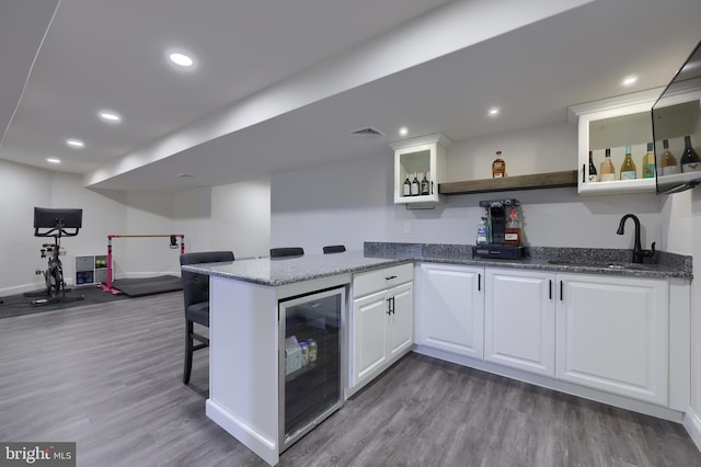 kitchen featuring white cabinets, a sink, a kitchen bar, dark stone counters, and wine cooler