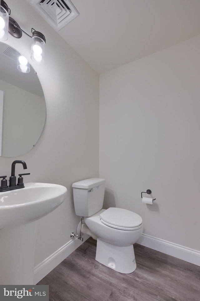 half bath featuring wood finished floors, visible vents, baseboards, and toilet