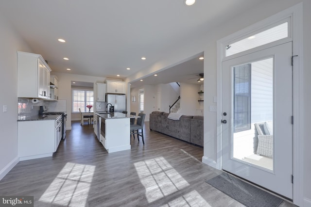 kitchen with open floor plan, a breakfast bar, white cabinetry, dark countertops, and a center island with sink