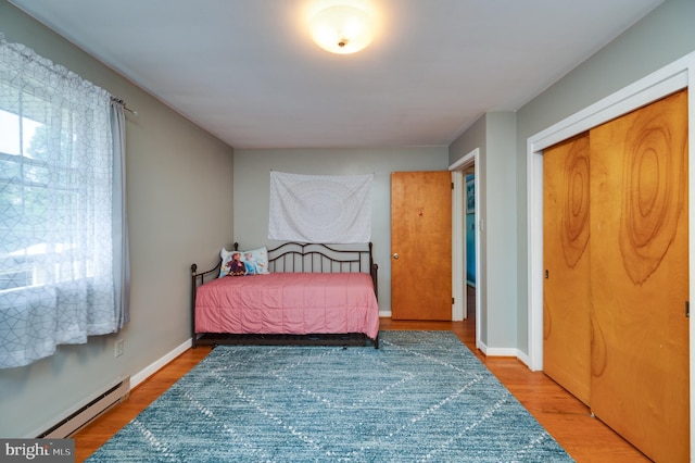 bedroom featuring a baseboard radiator, baseboards, a closet, and wood finished floors