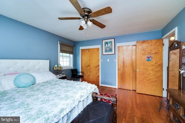 bedroom with baseboards, a ceiling fan, wood finished floors, and multiple closets