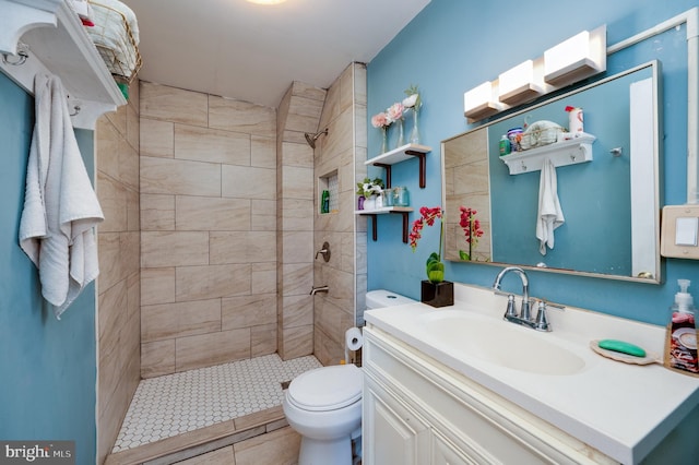 full bath featuring vanity, tiled shower, and toilet