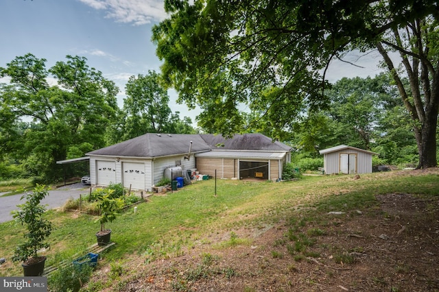 rear view of property featuring an outdoor structure, driveway, a storage shed, a yard, and an attached garage