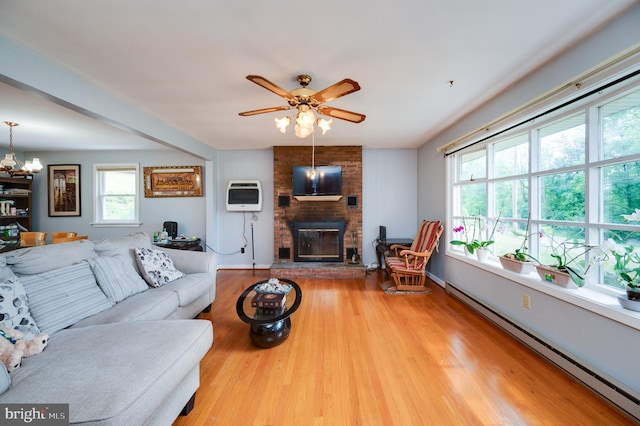 living room with heating unit, a baseboard heating unit, light wood finished floors, ceiling fan with notable chandelier, and a fireplace