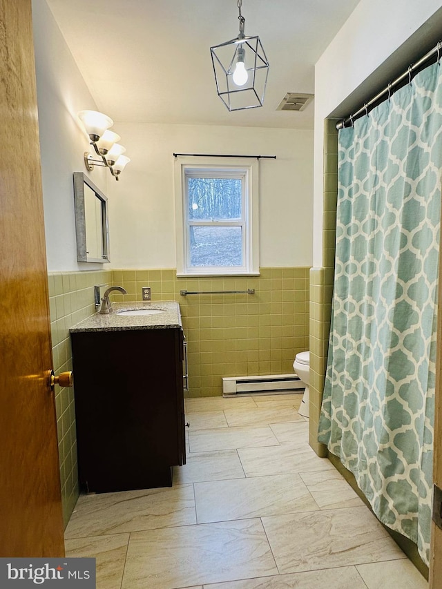 bathroom featuring a baseboard heating unit, visible vents, vanity, and tile walls