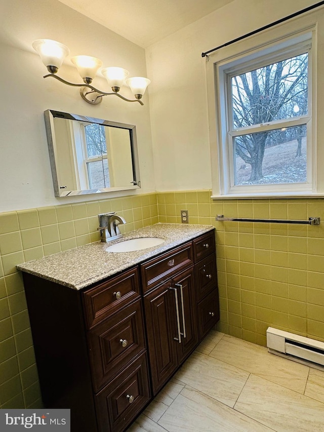 bathroom with a baseboard heating unit, vanity, wainscoting, and tile walls