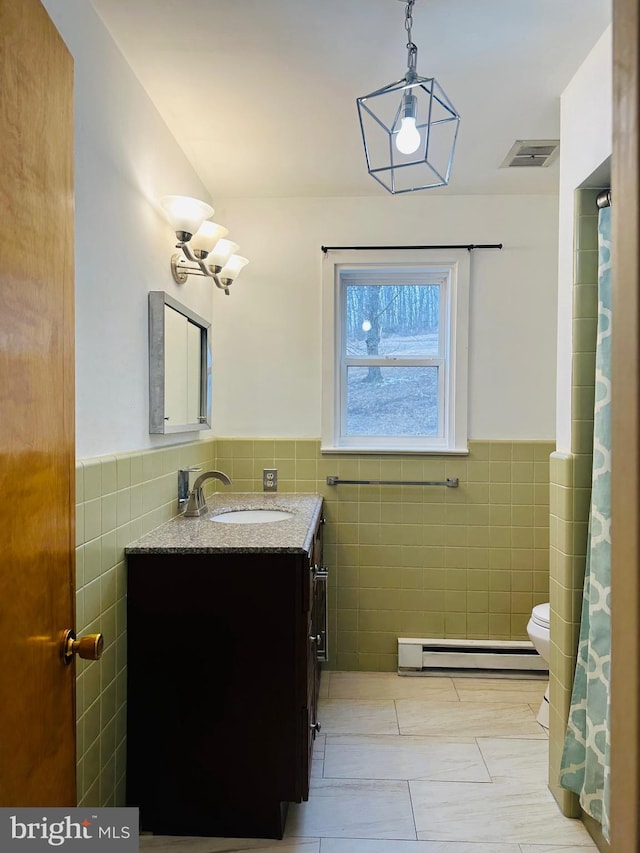 bathroom with vanity, tile walls, a baseboard radiator, visible vents, and wainscoting