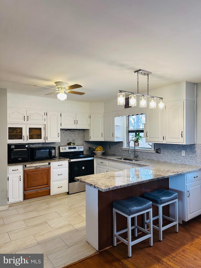 kitchen with a sink, stainless steel electric range oven, white cabinets, and black microwave