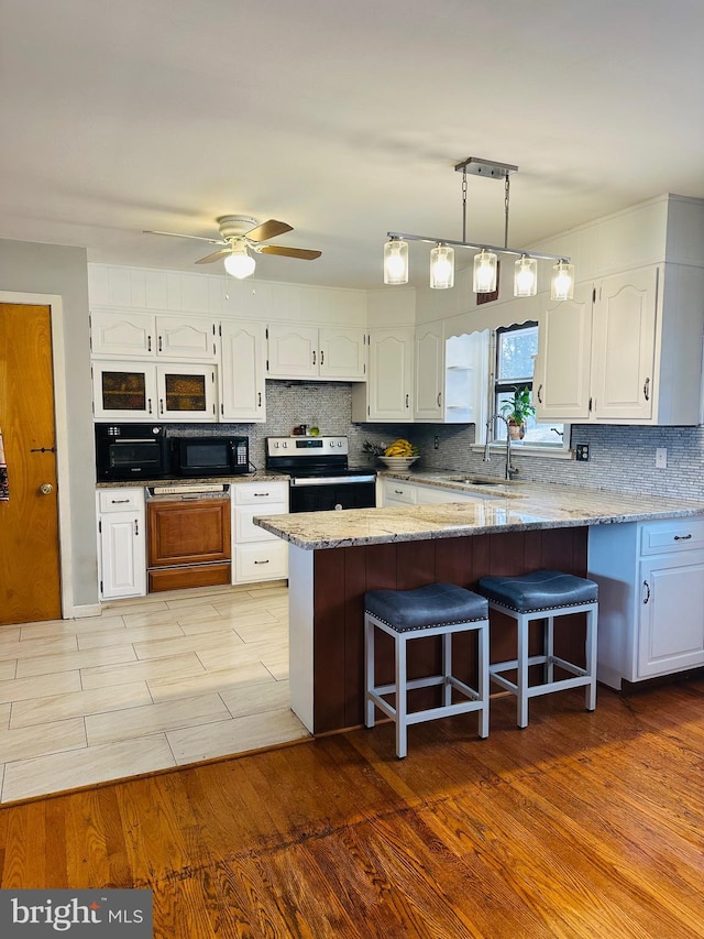 kitchen featuring a kitchen bar, a sink, white cabinetry, black microwave, and stainless steel range with electric stovetop