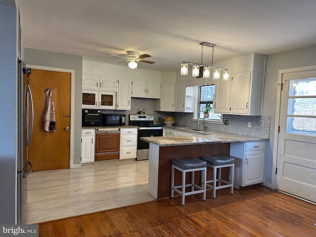 kitchen with appliances with stainless steel finishes, a breakfast bar, a sink, a peninsula, and white cabinetry