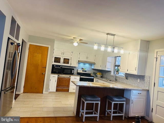 kitchen featuring appliances with stainless steel finishes, a breakfast bar, white cabinets, a peninsula, and under cabinet range hood