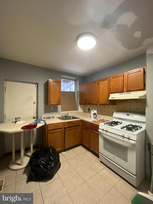 kitchen featuring white range with gas cooktop, light countertops, a sink, brown cabinetry, and under cabinet range hood