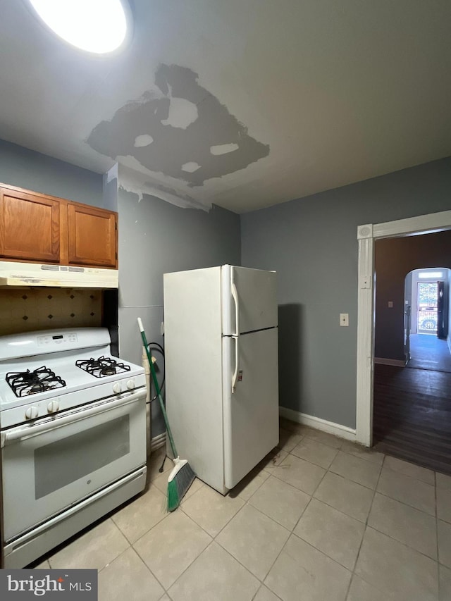 kitchen featuring arched walkways, under cabinet range hood, white appliances, light tile patterned flooring, and brown cabinetry