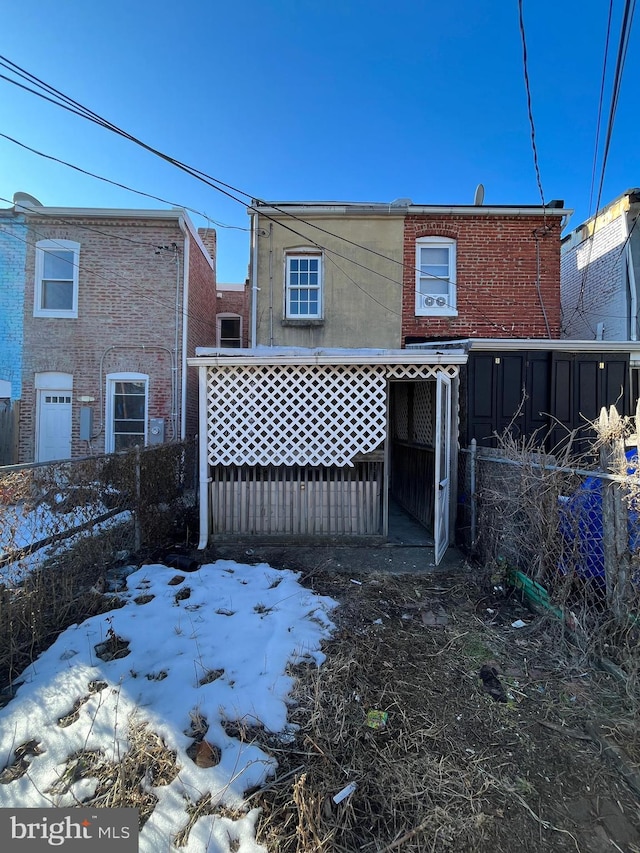 snow covered rear of property featuring brick siding and fence