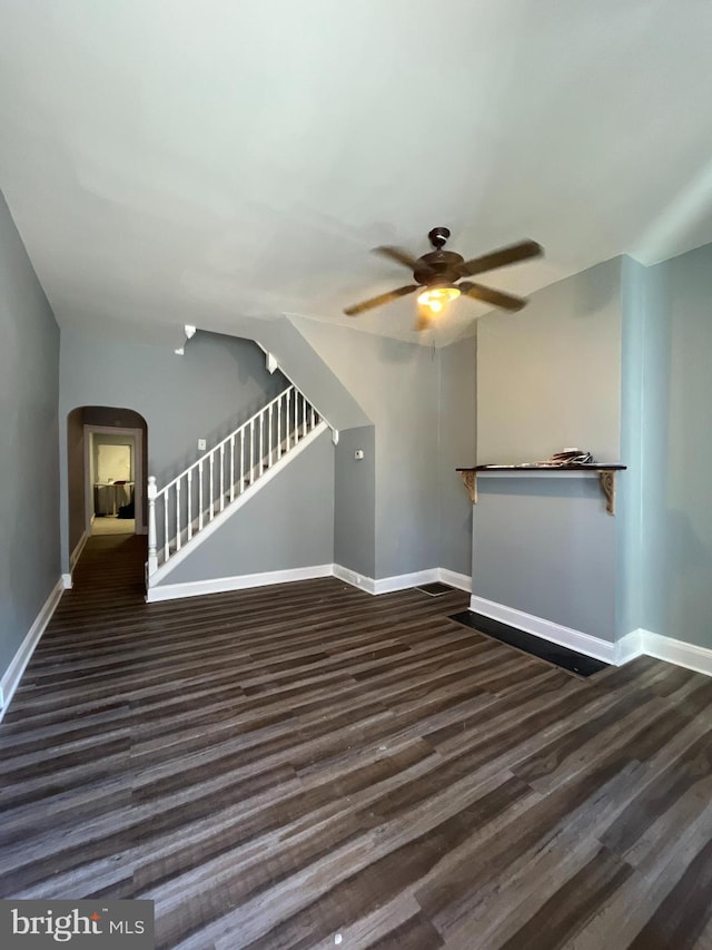 unfurnished living room with stairs, baseboards, arched walkways, and dark wood-type flooring