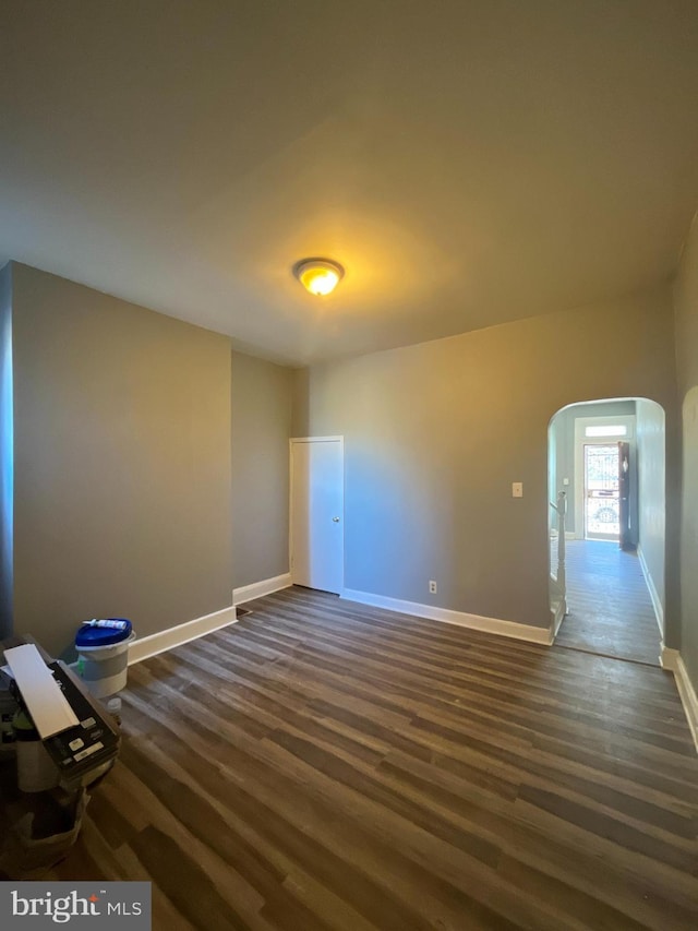 unfurnished room with dark wood finished floors, baseboards, and arched walkways