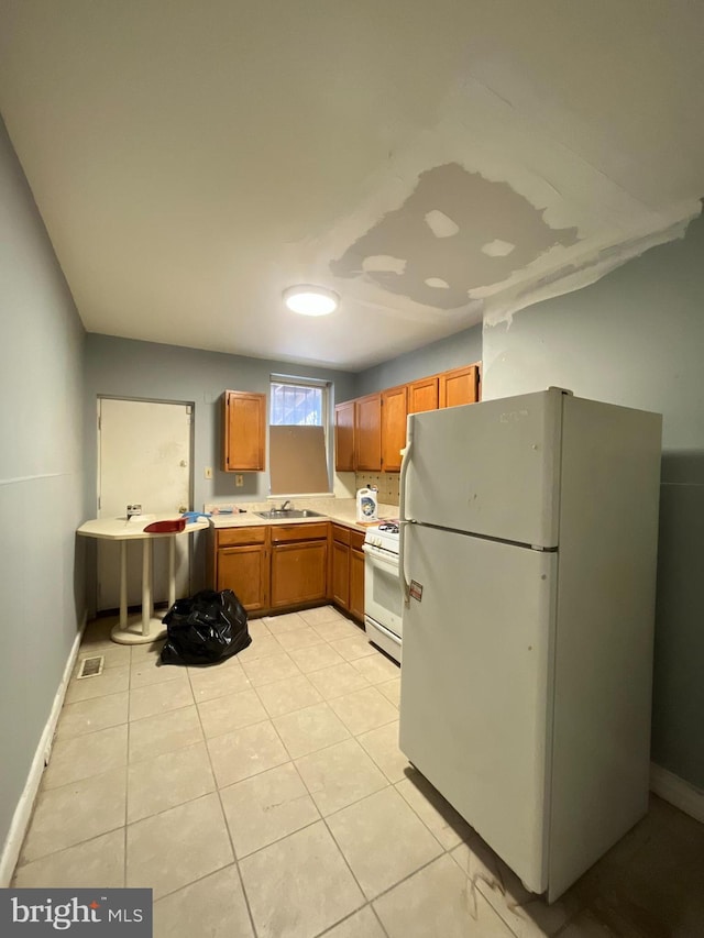 kitchen featuring a sink, light countertops, light tile patterned floors, white appliances, and brown cabinetry