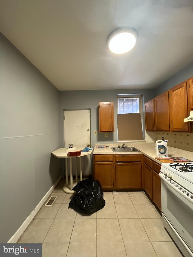 kitchen with brown cabinets, a sink, light countertops, white range with gas stovetop, and light tile patterned floors