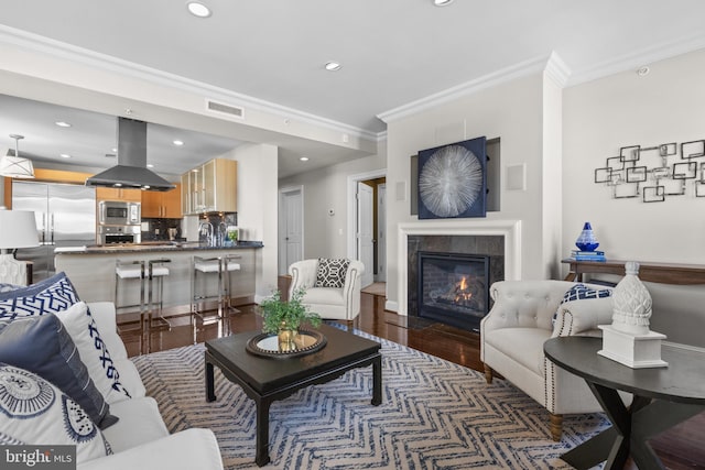 living area featuring a tile fireplace, recessed lighting, visible vents, dark wood finished floors, and crown molding