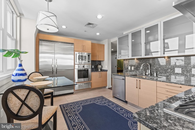 kitchen featuring pendant lighting, visible vents, a sink, built in appliances, and dark stone counters