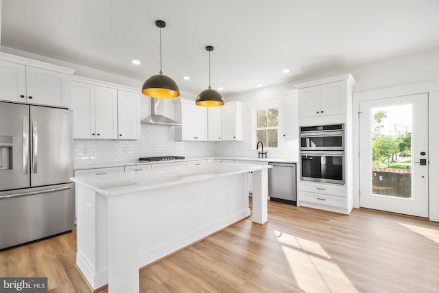 kitchen featuring white cabinetry, stainless steel appliances, decorative light fixtures, a kitchen island, and wall chimney range hood