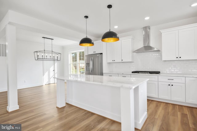 kitchen featuring hanging light fixtures, stainless steel fridge with ice dispenser, white cabinets, light stone counters, and wall chimney exhaust hood