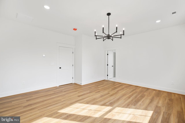 empty room featuring a notable chandelier and light wood-type flooring