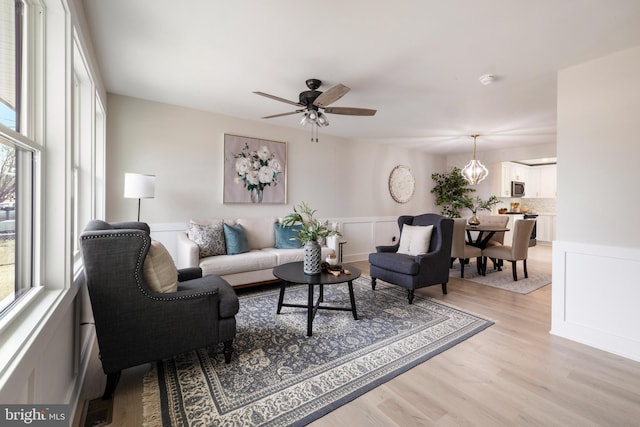 living room with light wood-type flooring, plenty of natural light, a decorative wall, and a notable chandelier