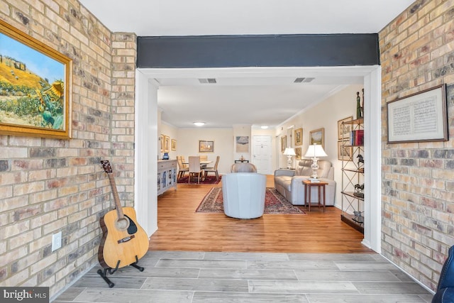 interior space featuring light wood finished floors, brick wall, visible vents, and crown molding