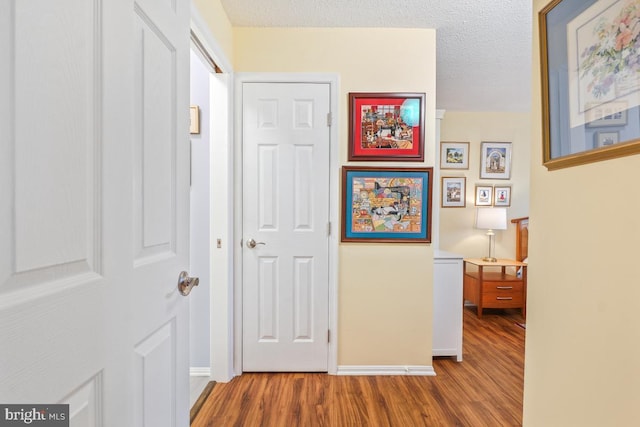 corridor featuring a textured ceiling, baseboards, and wood finished floors