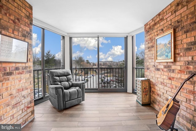 unfurnished room with expansive windows, brick wall, and light wood-style flooring