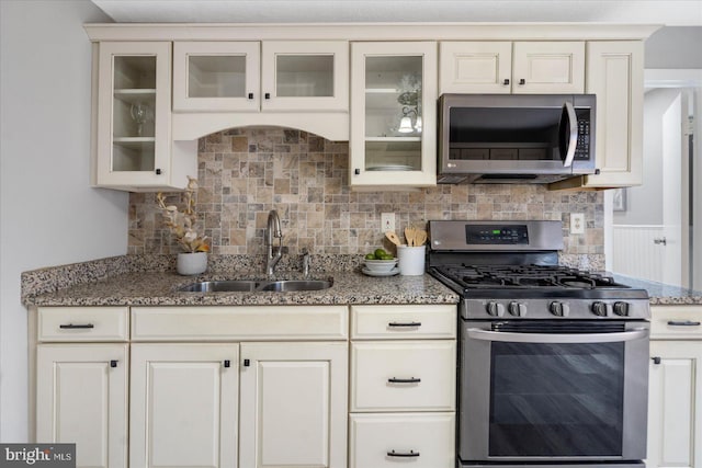 kitchen featuring stone countertops, decorative backsplash, glass insert cabinets, appliances with stainless steel finishes, and a sink