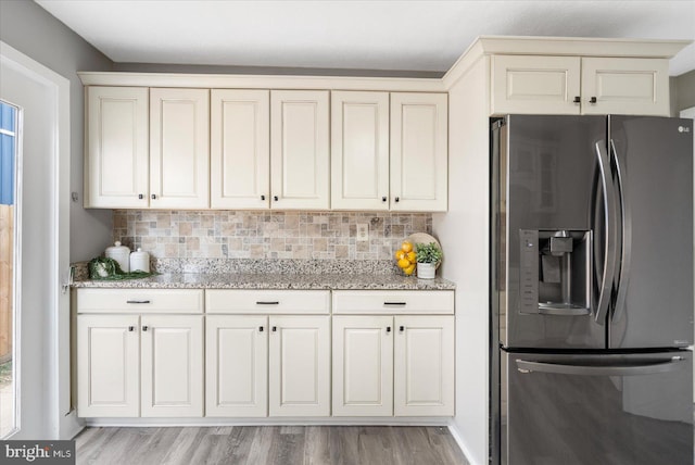 kitchen featuring light stone counters, light wood-style floors, stainless steel refrigerator with ice dispenser, and decorative backsplash