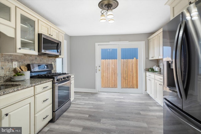 kitchen featuring cream cabinetry, appliances with stainless steel finishes, dark stone countertops, and glass insert cabinets