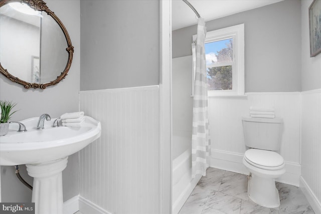 full bath featuring shower / tub combo, wainscoting, toilet, marble finish floor, and a sink