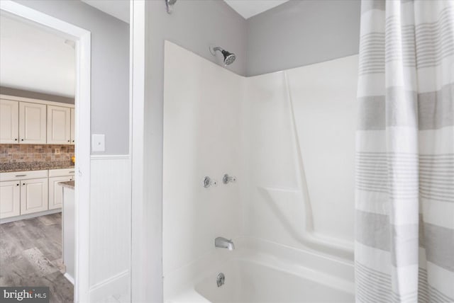 bathroom with a wainscoted wall, wood finished floors, vanity, backsplash, and shower / bathtub combination with curtain