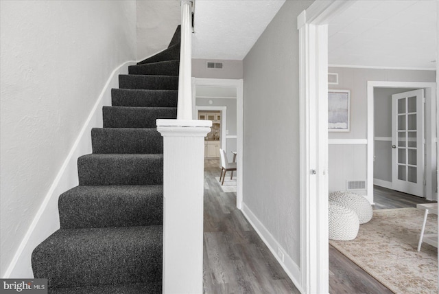 staircase with visible vents, wood finished floors, and a textured wall