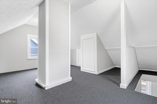 additional living space with lofted ceiling, dark carpet, and a textured ceiling