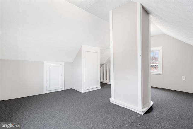 bonus room featuring vaulted ceiling, dark carpet, and a textured ceiling