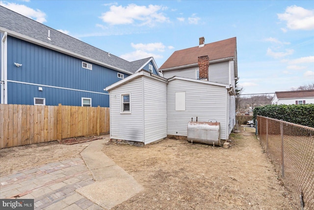 back of house with heating fuel, a fenced backyard, and a chimney