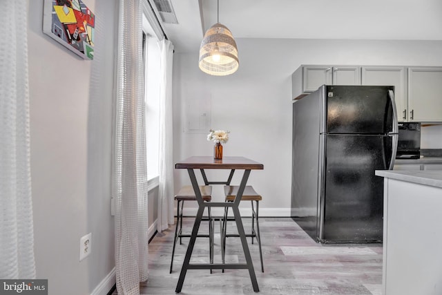 kitchen with freestanding refrigerator, light countertops, baseboards, decorative light fixtures, and light wood-type flooring