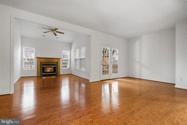 unfurnished living room with ceiling fan, a premium fireplace, baseboards, and wood finished floors