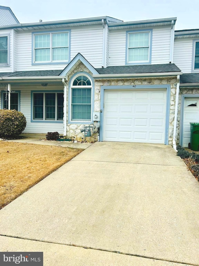 view of property featuring an attached garage, stone siding, concrete driveway, and roof with shingles