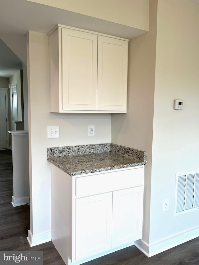 kitchen featuring visible vents, baseboards, white cabinets, dark wood finished floors, and dark stone counters