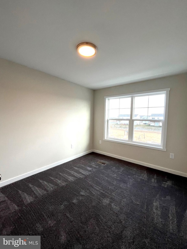 spare room with baseboards, dark carpet, and visible vents